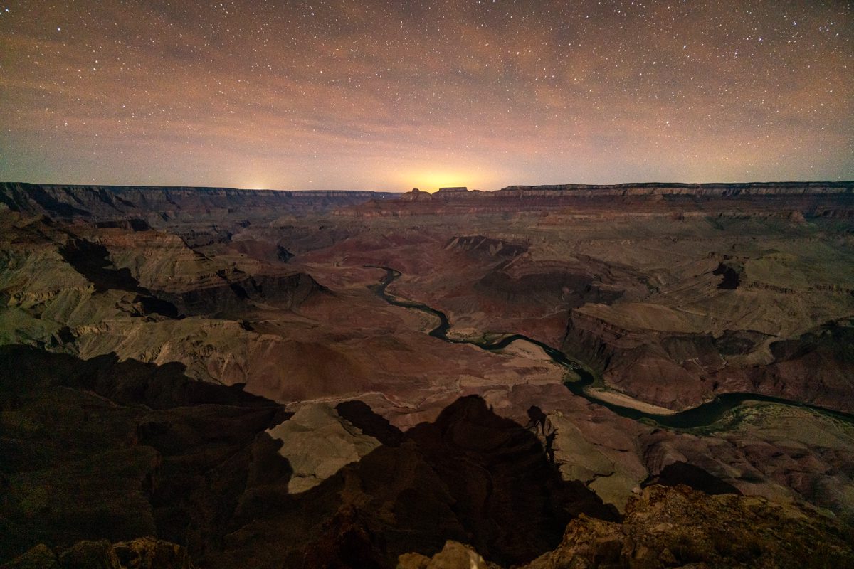The black triangluar moon shadow stretches towards the Colorado River with stars in the sky above.