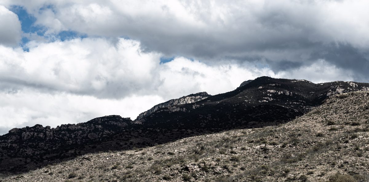 Cloudy skies, a distant shadowed ridgeline and desert hillsides in the foreground.