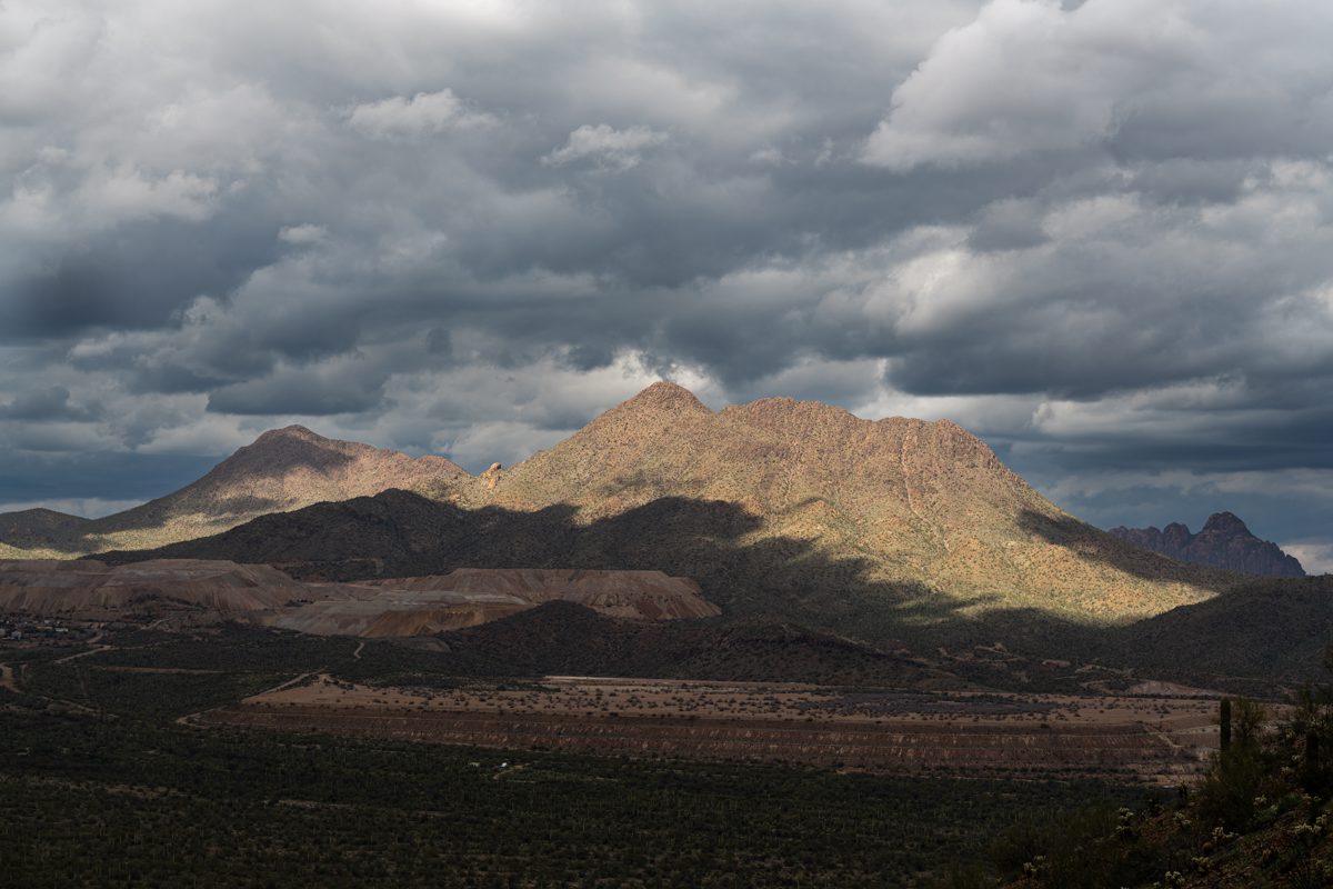 A window of sunlight highlights Silver Bell Peak and nearby ridgeline with storm clouds above and the Silver Bell Mine covered in shadows below.