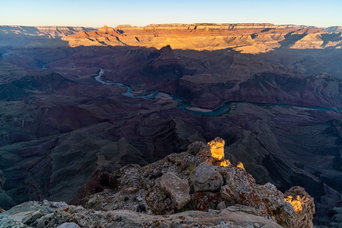 The sunrise light illuminates distant cliffs and the tip of a rock tower just below Comanche Point.