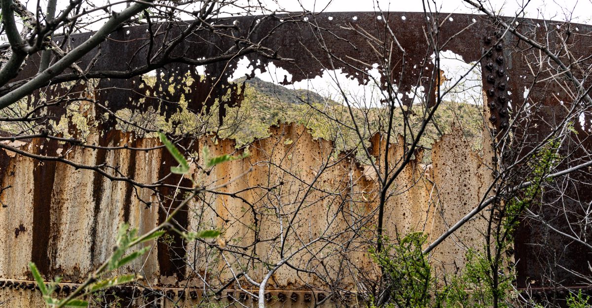 Brush in the foreground, a strangely rusted window in an old water tank and a unnamed peak in the Rincons visible thru the rusted.